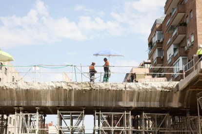 Dos albañiles se refugian del sol bajo una sombrilla.