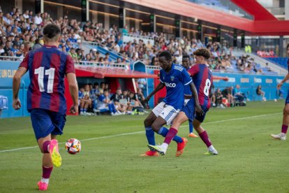 Musa Isah lucha por un balón ante la presión de un oponente, con el público de tribuna al fondo.