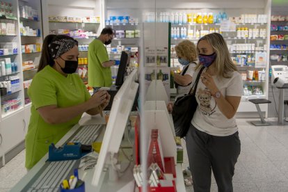 Trabajadores y clientes de una farmacia con mascarilla, que dejará de ser obligatoria en estos espacios. 