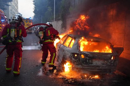 Els bombers apaguen les flames d’un cotxe durant els disturbis.