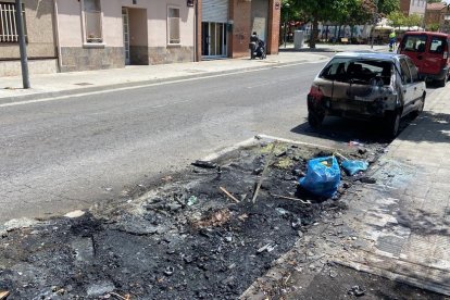 Les restes del contenidor cremat i el vehicle afectat pel foc al carrer Antoni Solé de Lleida.