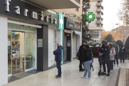 Imatge d’arxiu de diverses persones esperant per entrar en una farmàcia.