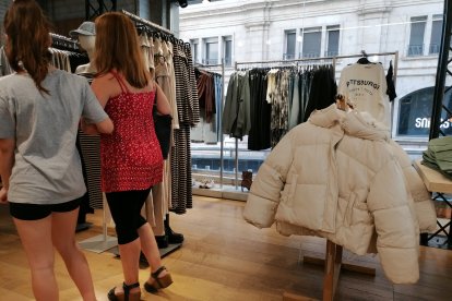 Dos clientes vestides d’estiu, al costat d’anoracs en una botiga de l’Eix Comercial.