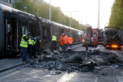 Operaris municipals netegen les restes d’un vehicle calcinat pels aldarulls de dijous.