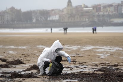 Un voluntari recollint pèl·lets en una platja de Gijón, ahir al migdia.