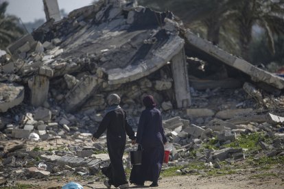 Dones palestines desplaçades passen al costat d’un edifici destruït al sud de la Franja de Gaza.