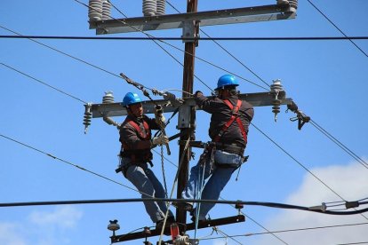 Dos treballadors amb un arnès de seguretat reparant cablatges en un pal telefònic.