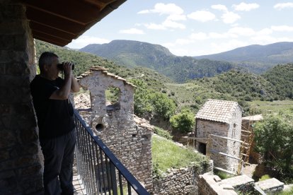 Jordi Canut observa aus des de l’única casa reconstruïda, amb l’església i una altra construcció al fons.