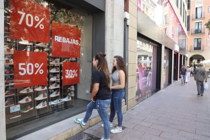 Dos joves mirant ahir un aparador d’una botiga de l’Eix Comercial que anuncia rebaixes.