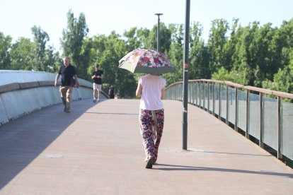 Una dona creuant ahir la passarel·la dels Camps Elisis amb un paraigua per protegir-se del sol.