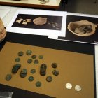 Dues monedes restaurades al costat d'altres peces pendents de tractar, vora la gerra de ceràmica on estaven amagades, al Laboratori d'Arqueologia de la UdL.