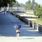 Una dona camina amb un paraigua pel carrer Jaume II de Lleida, vora la canalització del riu Segre, durant l'onada de calor.