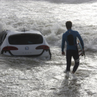Un surfista passa davant d’un cotxe a la platja de Vilassar de Mar.