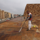 Un operari a la coberta de l’edifici netejant la pedra amb aigua a pressió.