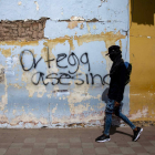 Un joven con la cara tapada camina delante de una pintada en Nicaragua.