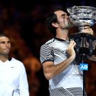 Roger Federer besa el trofeu aconseguit a Melbourne amb Rafa Nadal al fons de la imatge.
