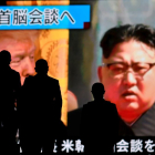 Personas pasan por delante de una pantalla con la imagen de los líderes de EEUU y Corea del Norte.