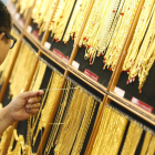 Un hombre sostiene collares de oro en un local de venta de oro. 