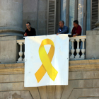 Tres operarios colocan de nuevo el lazo amarillo en la fachada del ayuntamiento de Barcelona.