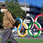 Un hombre protegido por una máscara pasa junto a los anillos olímpicos instalados en Tokio.