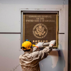 Un hombre quita la placa a la entrada del consulado de EEUU.