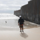 Un hombre parado frente al muro construido en la frontera sur de Estados Unidos.