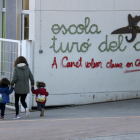 Una madre acompaña a sus hijos a la escuela Turó del Drac de Canet de Mar. Una pintada reclama la enseñanza en catalán en la fachada del centro.