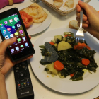 Un menor menja amb un mòbil en una mà.