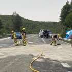 Bombers netejant la carretera, que va estar unes tres hores tallada, i al fons un dels turismes implicats.