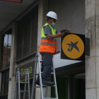 Un operario colocando el logotipo de CaixaBank en la oficina situada en el número 116 de la Rambla del Poblenou de Barcelona, anteriormente una oficina de Bankia.
