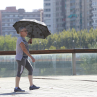 Una mujer se protege del sol con un paraguas, ayer, para cruzar la pasarela sobre el río Segre.