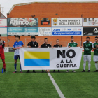 Jugadores de ambos equipos posan antes del partido con una pancarta de rechazo a la guerra.