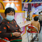 Una dona amb una mascareta amb el mòbil en un centre comercial.