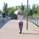Una dona creuant ahir la passarel·la dels Camps Elisis amb un paraigua per protegir-se del sol.