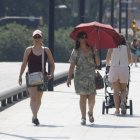 Dos vianants es protegeixen del sol amb paraigua i gorra a Lleida. - E.B.D.