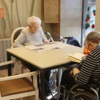 Una dona llegeix el diari en una residència al costat d’un altre resident amb un llibre. - ACN