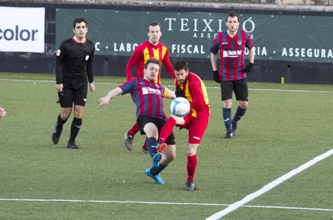 Dos jugadors pugnen pel control de la pilota en presència de l’àrbitre i d’altres futbolistes.