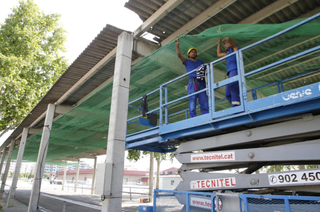 Operarios instalan un toldo provisional debajo del fibrocemento.