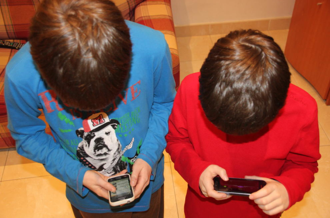 Imagen de dos niños jugando con el teléfono móvil en casa. 