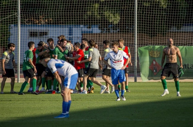 Adrià Fernández, sin camiseta, celebra con sus compañeros del Ascó el ascenso mientras en primer plano dos jugadores del Mollerussa muestran su abatimiento.