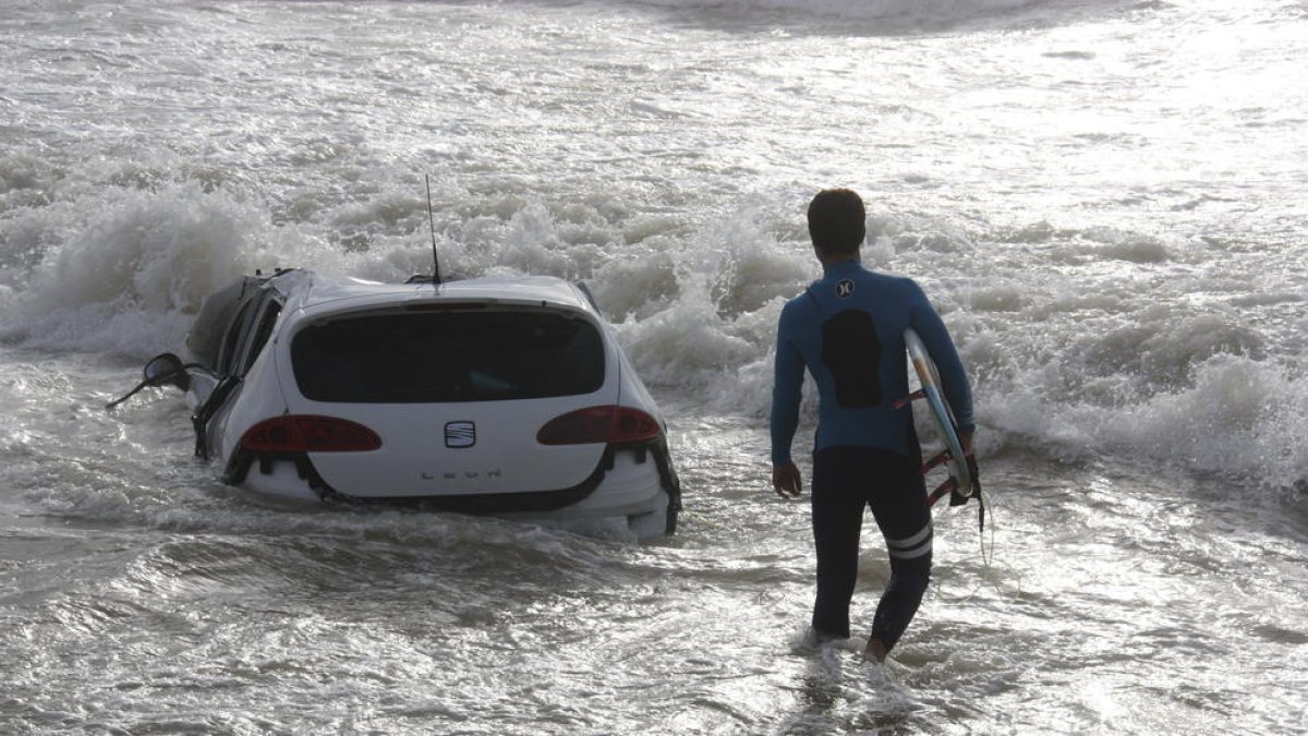 Un surfista passa davant d’un cotxe a la platja de Vilassar de Mar.