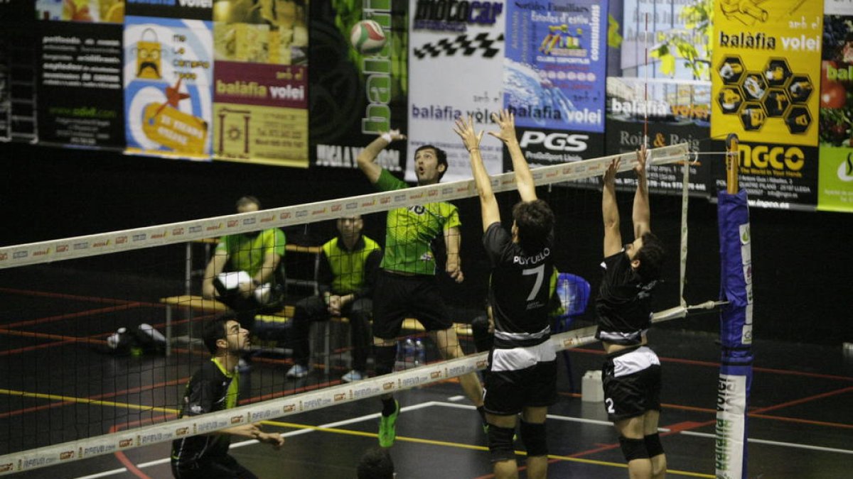 Un jugador de La Nuit Balàfia Vòlei remata ante la oposición de dos rivales.
