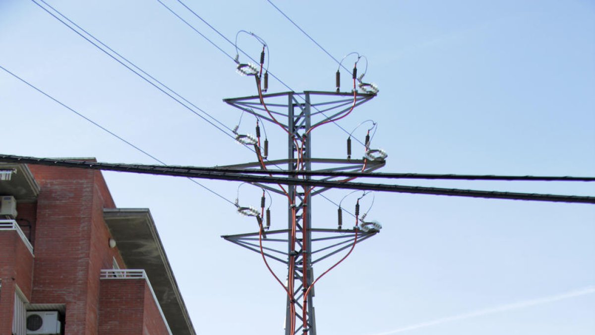 Una torre eléctrica, junto a unas viviendas y en medio de la acera.