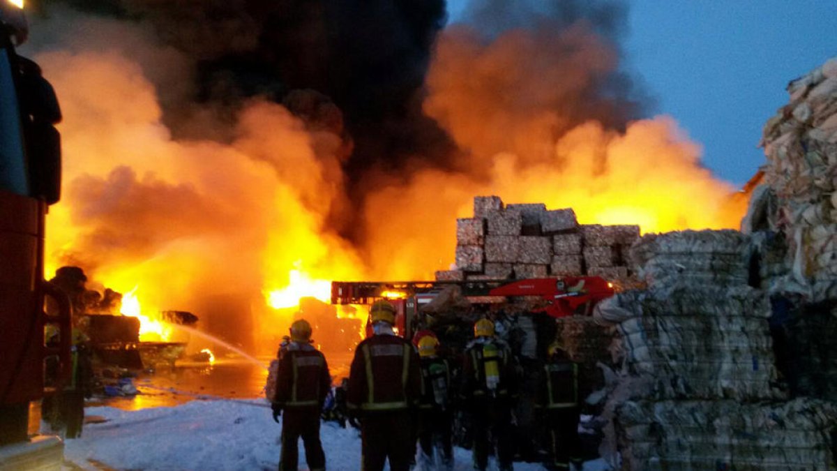 Bomberos observan las llamas de la empresa de Girona.