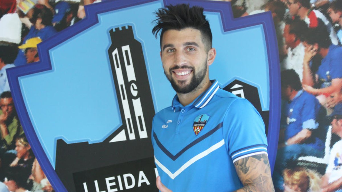 El nuevo jugador del Lleida Esportiu, Marc Trilles, posa ya con la equipación del club y junto al escudo.