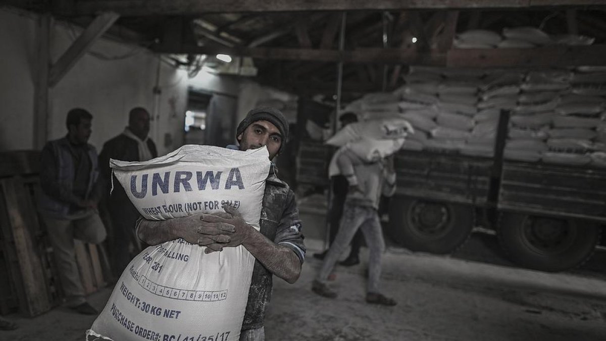 Un refugiado palestino lleva un saco con harina en un campamento de refugiados de Gaza.