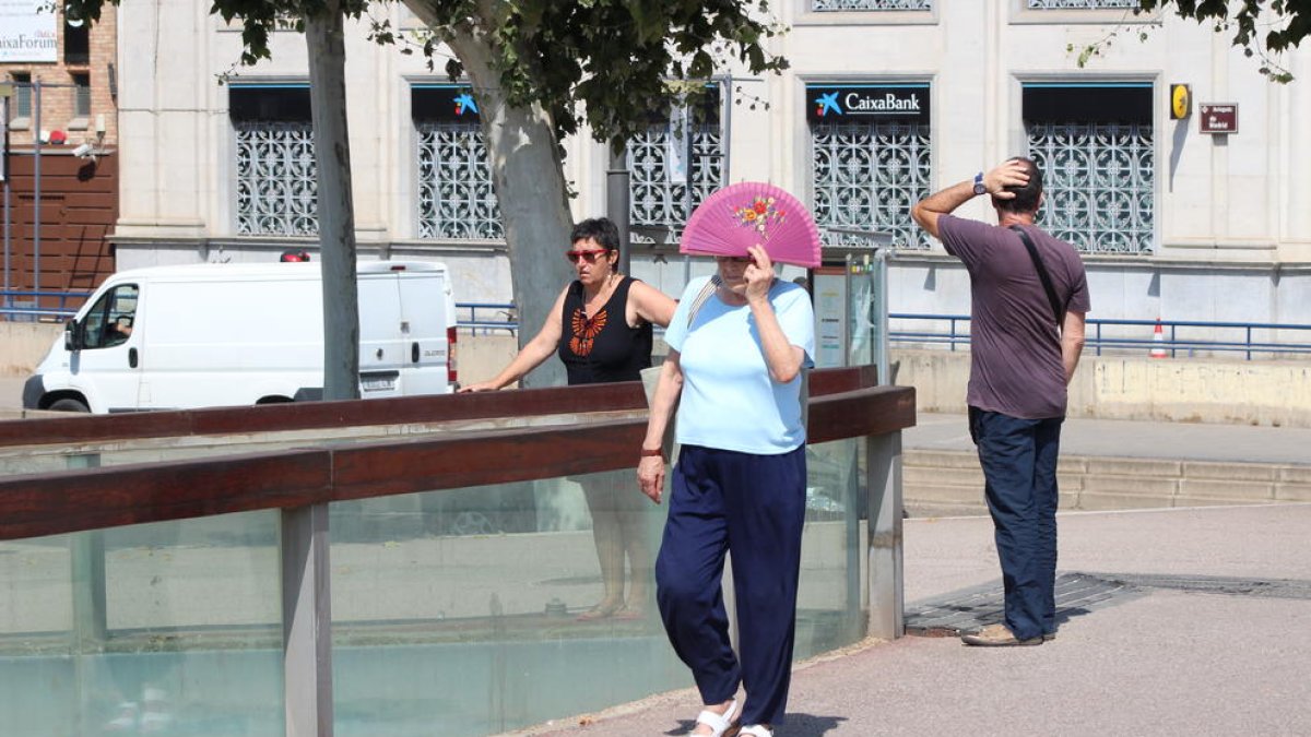 Una mujer se protege del sol con un abanico al cruzar la pasarela Liceu Escolar este verano.