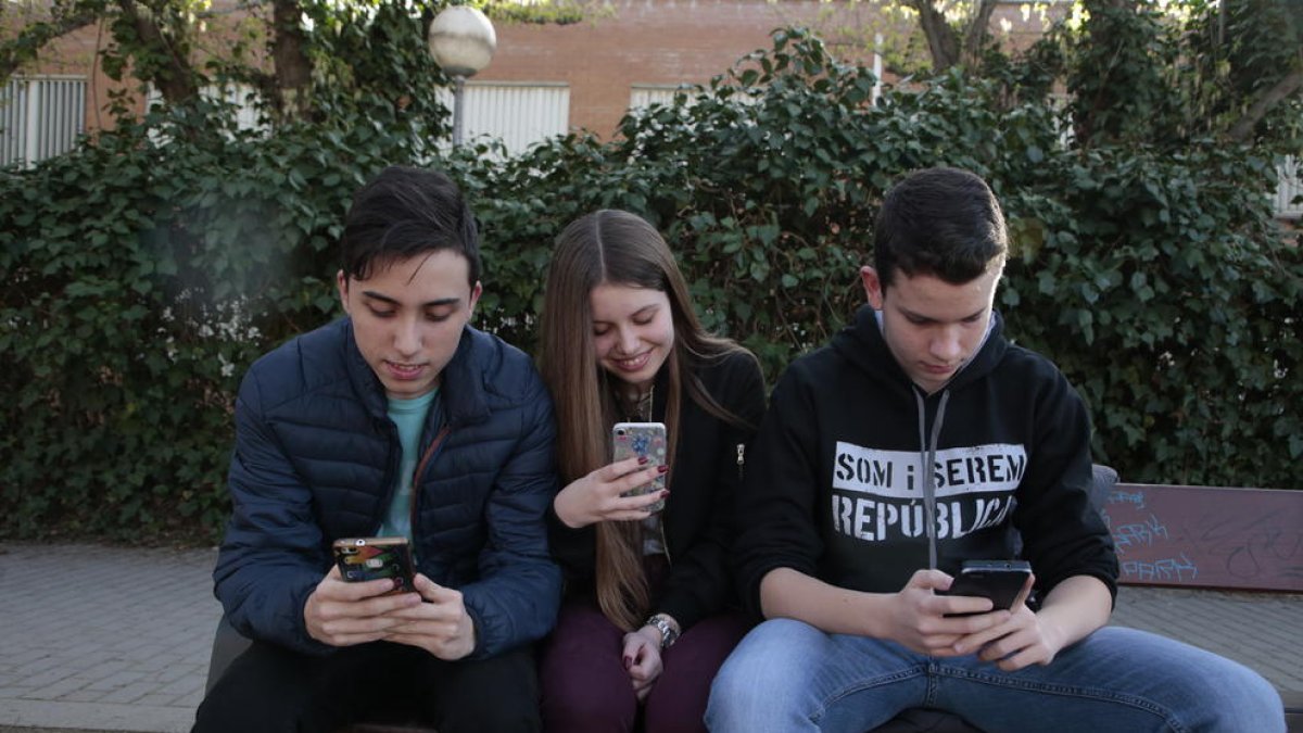 Tres amigos de Pardinyes, navegando por la red con sus móviles ante el instituto Josep Lladonosa.