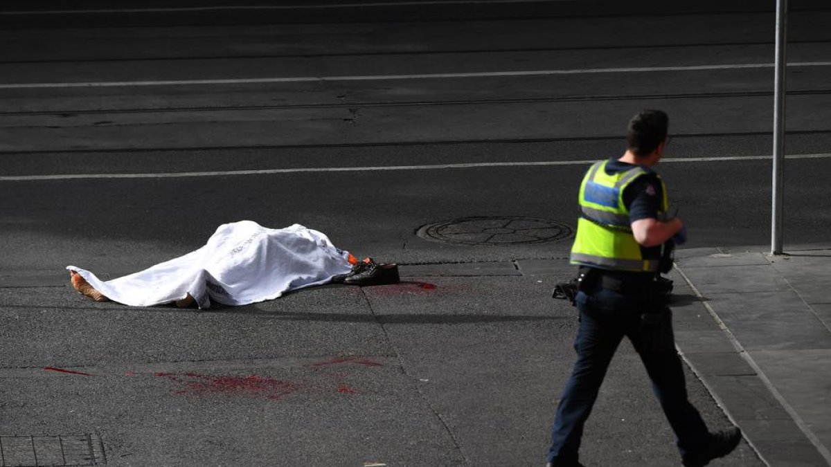 El cadàver de la víctima, a terra, custodiat per un policia.