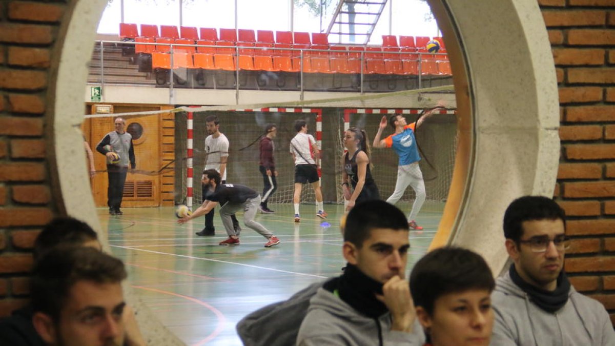 Alumnos de Inefc durante una clase teórica y tras ellos otros practicando voleibol en el pabellón.